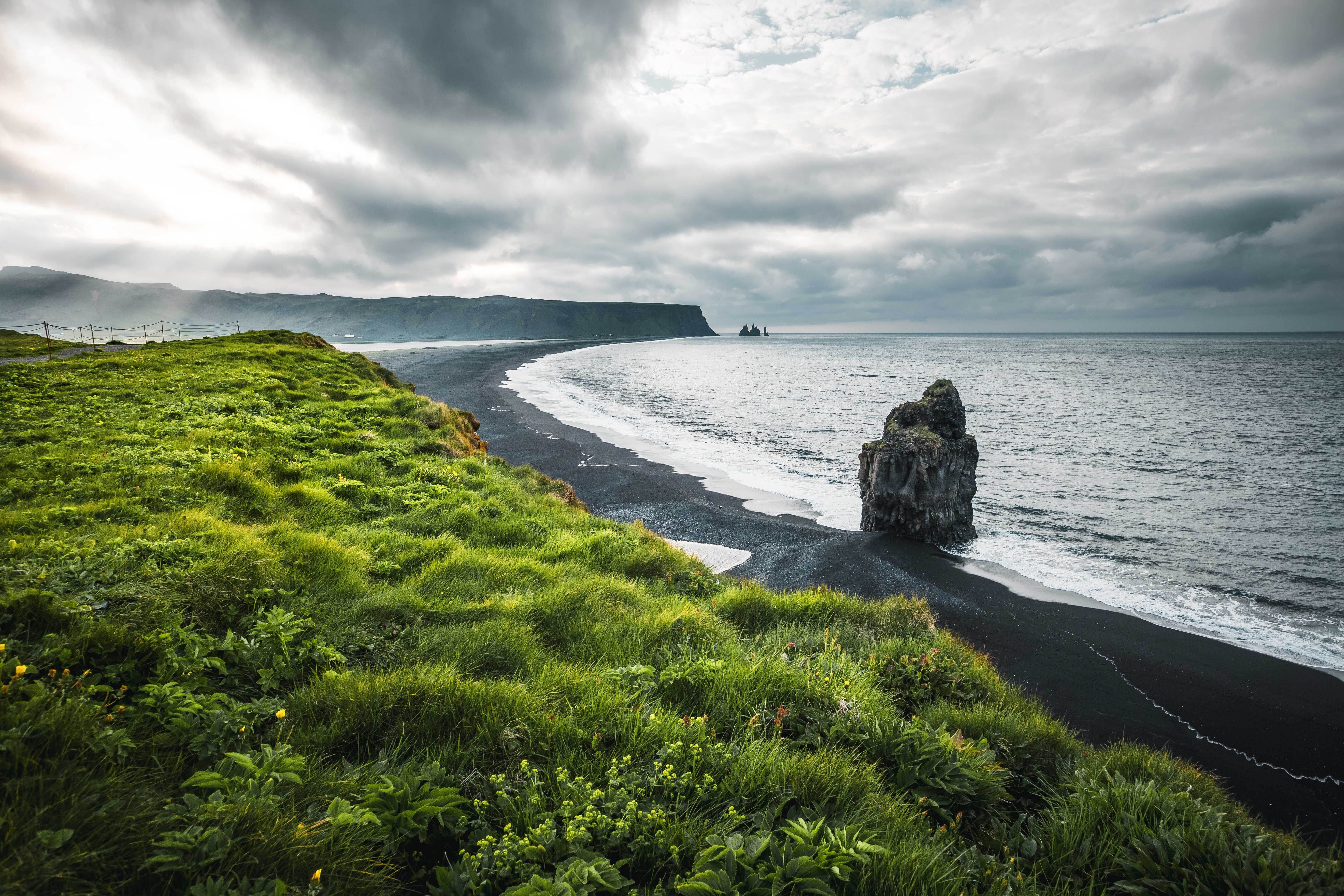 Dramatic green clifftop over a black-sand beach and sea stack