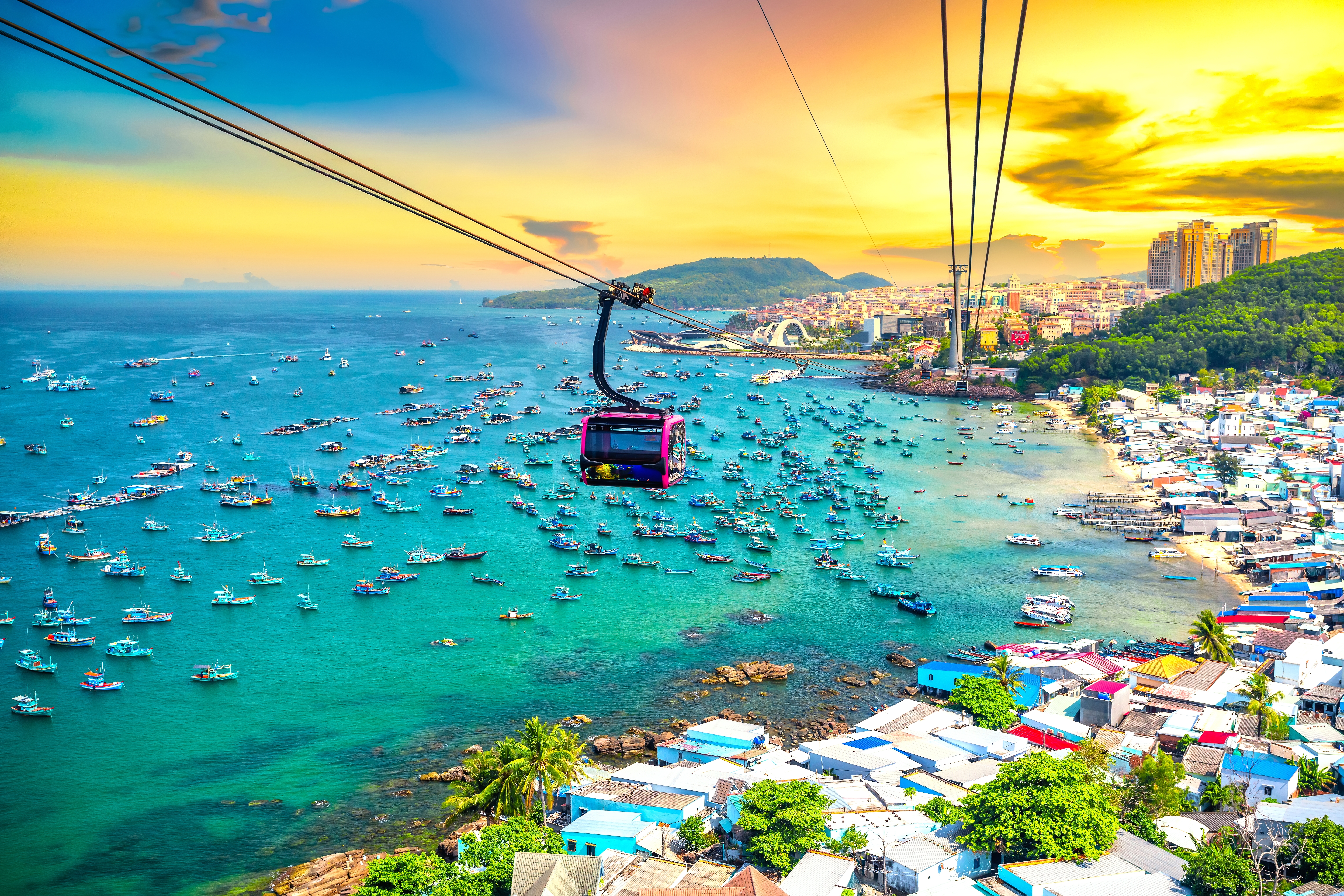 Cable car gliding over a turquoise bay full of boats at sunset